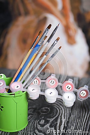 Brushes and paints for painting in a bucket. Drawing by numbers. Against the background of a fragment of a painted picture. The Stock Photo