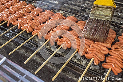 Brushing marinade on skewered Chicken small intestine, or locally known in the Philippines as isaw, on a charcoal grill Stock Photo