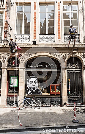 Brussels Old Town - Belgium Two workers on safety cables putting decoration on a facade of the music village shop Editorial Stock Photo