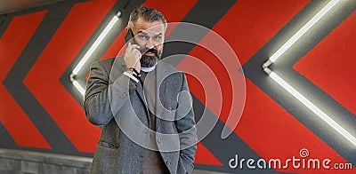 brutal adult male businessman speaks on a mobile phone against the background of a bright wall with red arrows Stock Photo