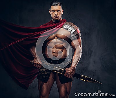 Brutal ancient Greek warrior with a muscular body in battle equipment posing on dark background. Stock Photo