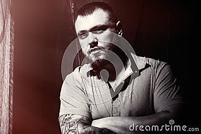 Brutal bearded man with a tattoo on his arm, a portrait of a man in dramatic light against a brown wooden wall, attractive bearded Stock Photo