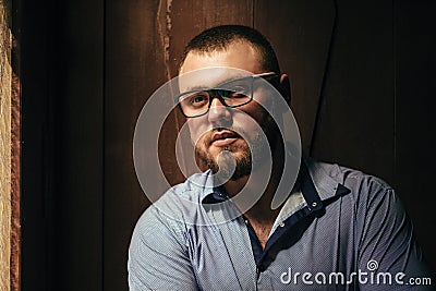 Brutal bearded man with a tattoo on his arm, portrait of a man in dramatic light against a brown wooden wall, bearded male with ta Stock Photo