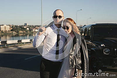 Brutal couple, the bride and groom, with a bat in leather jackets near the car on the road Stock Photo