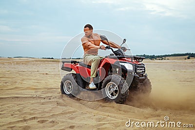Brutal man poses on atv in desert sands, quadbike Stock Photo