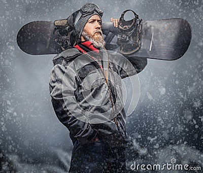 Brutal redhead snowboarder with a full beard in a winter hat and protective glasses dressed in a snowboarding coat Stock Photo
