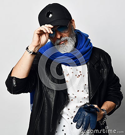 Brutal senior rich man in leather jacket and long blue scarf stands with gloves in arms and holds the visor Stock Photo