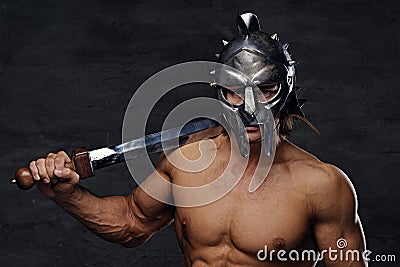 A man in a silver gladiator helmet holds an iron sword. Stock Photo