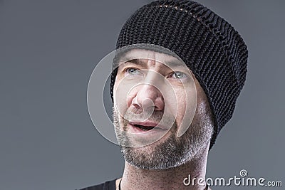 Brutal unshaven man in a black knitted hat. Grey background. Close-up Stock Photo