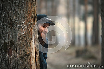 A brutal young man with a huge beard in sunglasses and a cap in the woods at sunset. Stock Photo