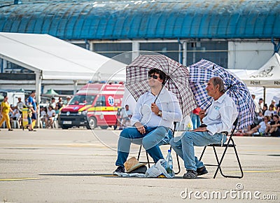 Two men with umbrellas sitting on chairs in the sun. Summer heat concept Editorial Stock Photo