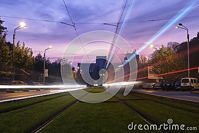 Car headlights and stoplights along a green tramway track on Liviu Rebreanu street, at sunset, with purple and pink skies. Editorial Stock Photo