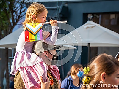 Young girl on the back of her father holding The rainbow flag, symbol of LGBT and queer pride at Editorial Stock Photo