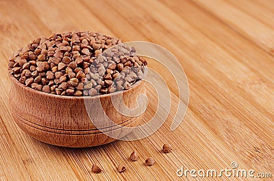 Buckwheat brown in wooden bowl on brown bamboo board, closeup. Stock Photo