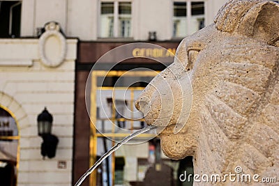 Stone lion head sculpture fountain. famous patisserie sweetshop in the background Editorial Stock Photo