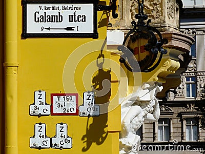 White street name sign in Budapest, many utility and service indicator plates mounted on the yellow exterior wall Editorial Stock Photo