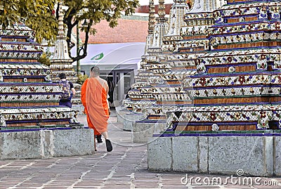 Buddhist monk with traditional orange clothes walking inside of buddha temple between ornaments and mosaic columns in Bangkok, Tha Editorial Stock Photo
