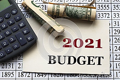 2021 BUDGET - words on white paper against the background of a table of numbers with a calculator and banknotes Stock Photo