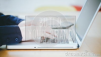 Build Your Brand, text over young man typing on laptop at desk Stock Photo