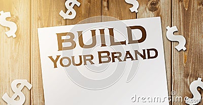 Build Your Own Brand words on a page and paper dollar signs around on wooden table. Branding rebranding marketing business concept Stock Photo