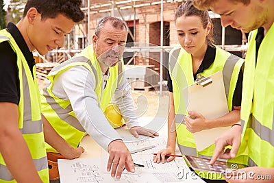 Builder On Building Site Discussing Work With Apprentice Stock Photo