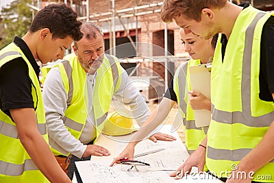 Builder On Building Site Discussing Work With Apprentice Stock Photo