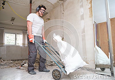 Builder collecting construction debris in a bag, and carrying in a hand trolley Stock Photo