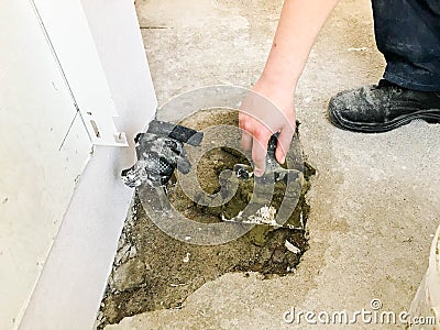 Builder hands with a metal spatula plaster the wall, pours the screed with plaster, tile glue, cement for the repair Stock Photo