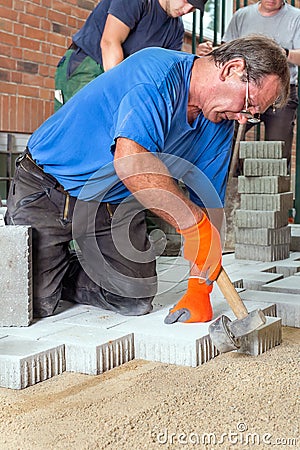 Builder laying paving stones with his team. Stock Photo