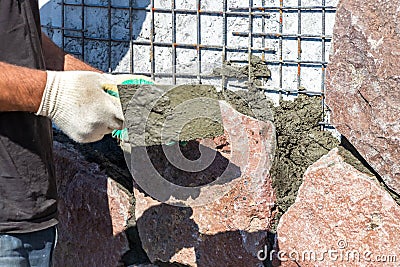 Builder - mason hands placing stones on a wall using a spatula with cement, outdoors Stock Photo