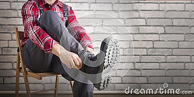 Builder putting on shoes for work near brick wall. Stock Photo