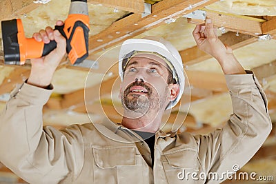 Builder using cordless drill on wooden ceiling joists Stock Photo