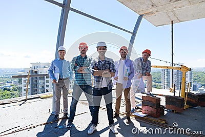 Builders Team Leader With Group Of Apprentices At Construction Site Over City View Background, Happy Smiling Engineers Stock Photo