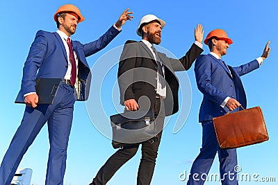 Builders walk and wave at someone on blue sky background. Stock Photo