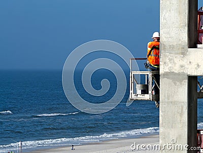 Building construction worker high over ocean beach Editorial Stock Photo