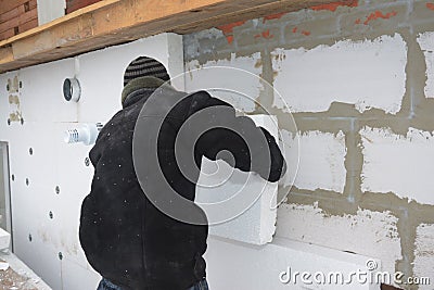 A building contractor is installing an external solid wall insulation fixing insulating polystyrene panels to the wall with Stock Photo