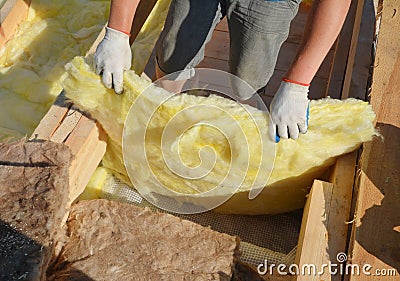 A building contractor is laying mineral wool sheets in protective gloves on the rooftop for thermal insulation, energy efficiency Stock Photo