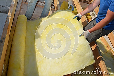 A building contractor in protective gloves is unrolling fiberglass insulation before its installation on the roof attic Stock Photo