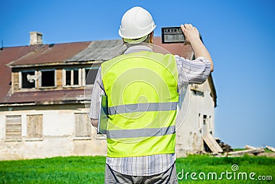 Building inspector filming on tablet PC near old abandoned, damaged house on grass field Stock Photo