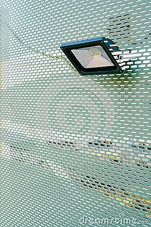 Building LED floodlight. Rectangular floodlight. A small spotlight hangs on a green wall with perforation. Stock Photo