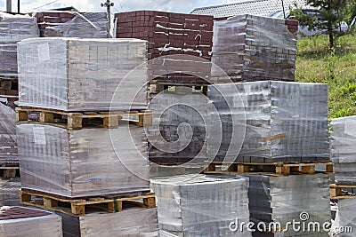 Building materials on pallets, red bricks paving stone. Warehouse building materials in the open. Bricks and building Stock Photo