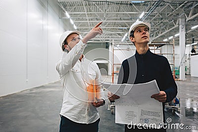 Two industrial engineers wearing safety hard hat have meeting on commercial building structure Stock Photo