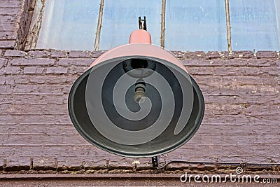 Bulb in a large open circular lampshade of metal on a brick wall Stock Photo