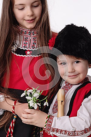 Bulgarian kids boy and girl in traditional folklore costumes with spring snowdrops, martenitsa symbol of Baba Marta Stock Photo