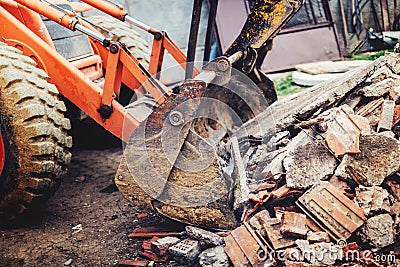 Bulldozer demolishing concrete walls of small building and gathering debri, loading into dumper trucks Stock Photo