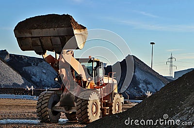 Bulldozer with raised hydraulic boom and the bucket full of earth, between gravel heaps of the open mine Stock Photo