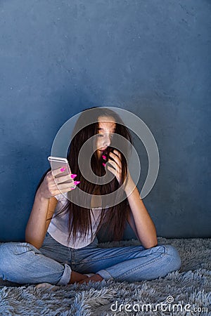 Bullying online concept. Alone worried girl sitting at home on the bed with cellphone. Stock Photo