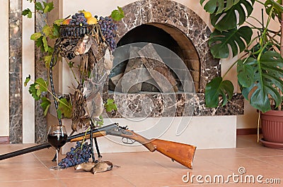 Bunch of birds, grape, wine and rifle on background of the fireplace. Stock Photo