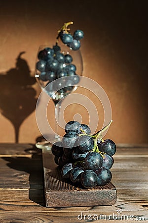 A bunch of blue dark grapes and a wine glass on a dark background in the conditions of artificial hard lighting close up. In a gla Stock Photo