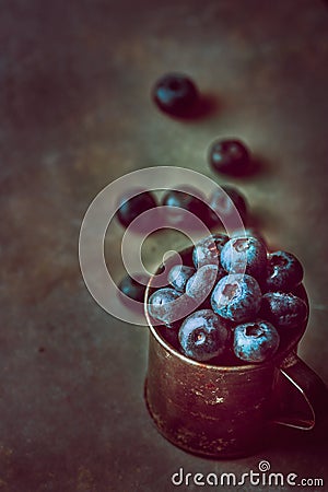 Bunch of blueberried in rusty metal jug on dark stone concrete background. Scattered berries. Creative toned image with copy space Stock Photo